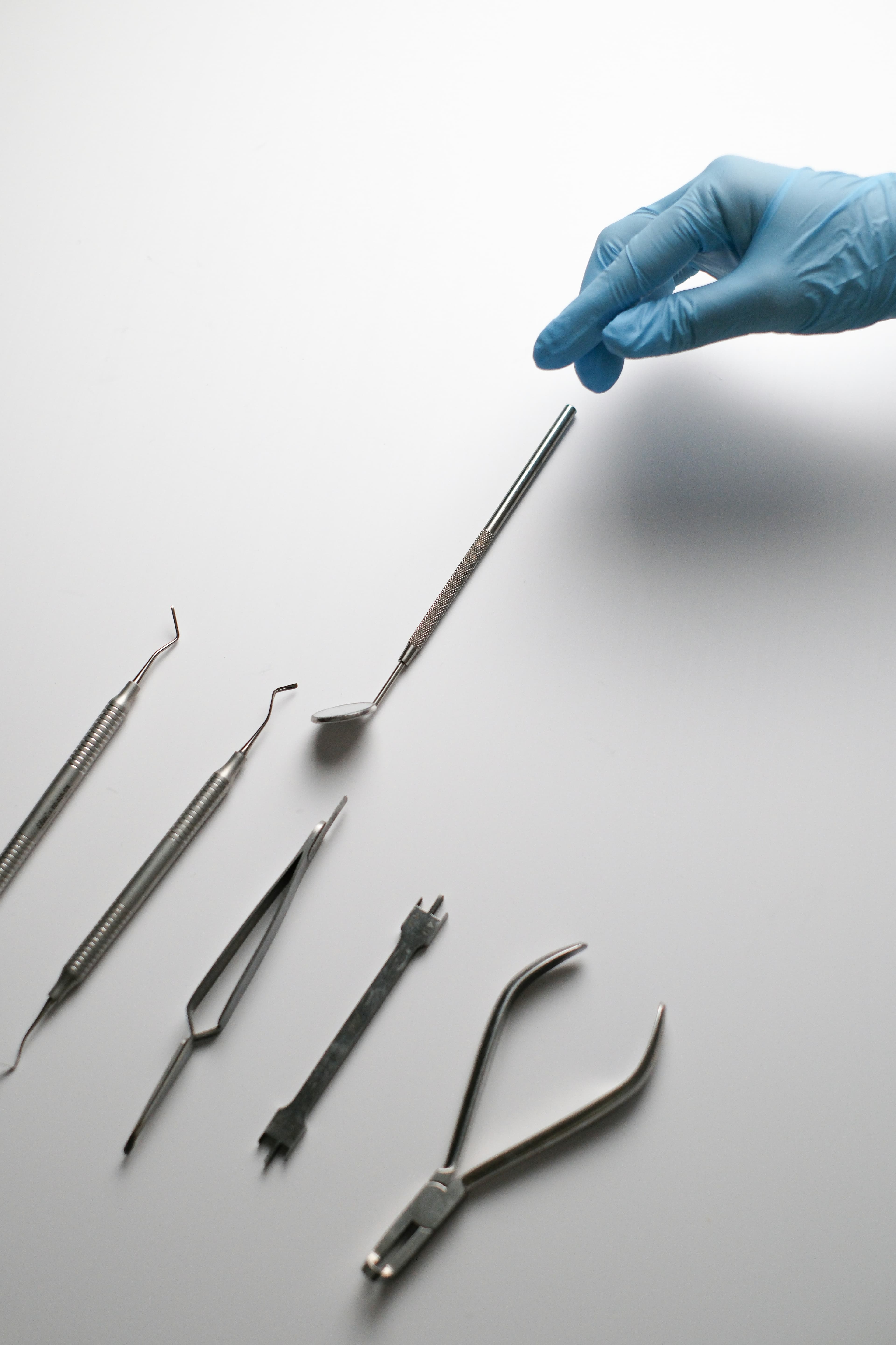 A blue-gloved hand reaching for a steel instrument laid out with others on a pale surface.